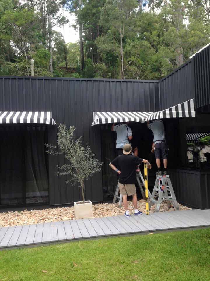 A Group Of People Are Working On A Black Building With A White Awning — Homemakers Lifestyle In Nambour, QLD