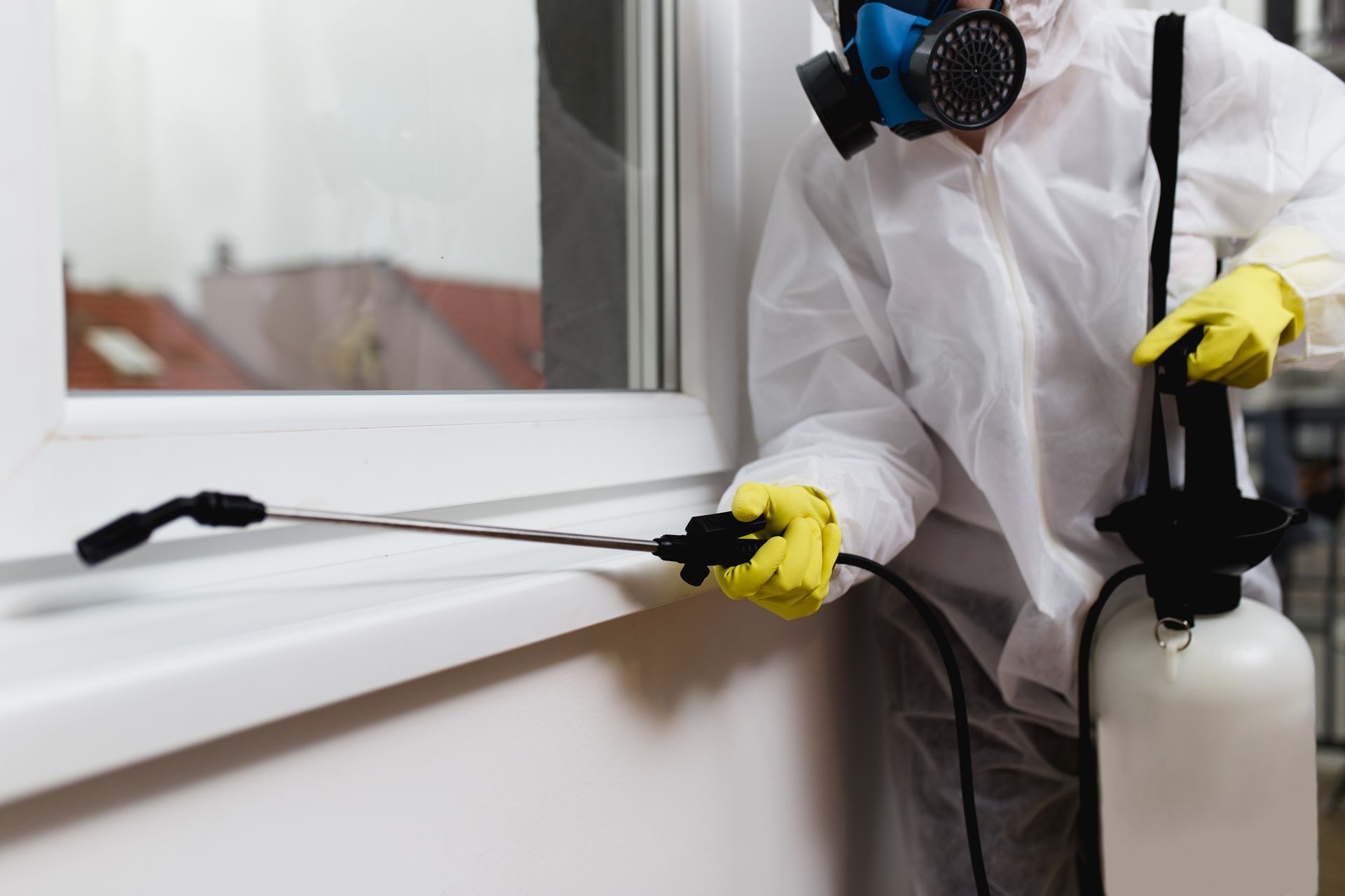 Person in hazmat suit spraying insecticide near a window.