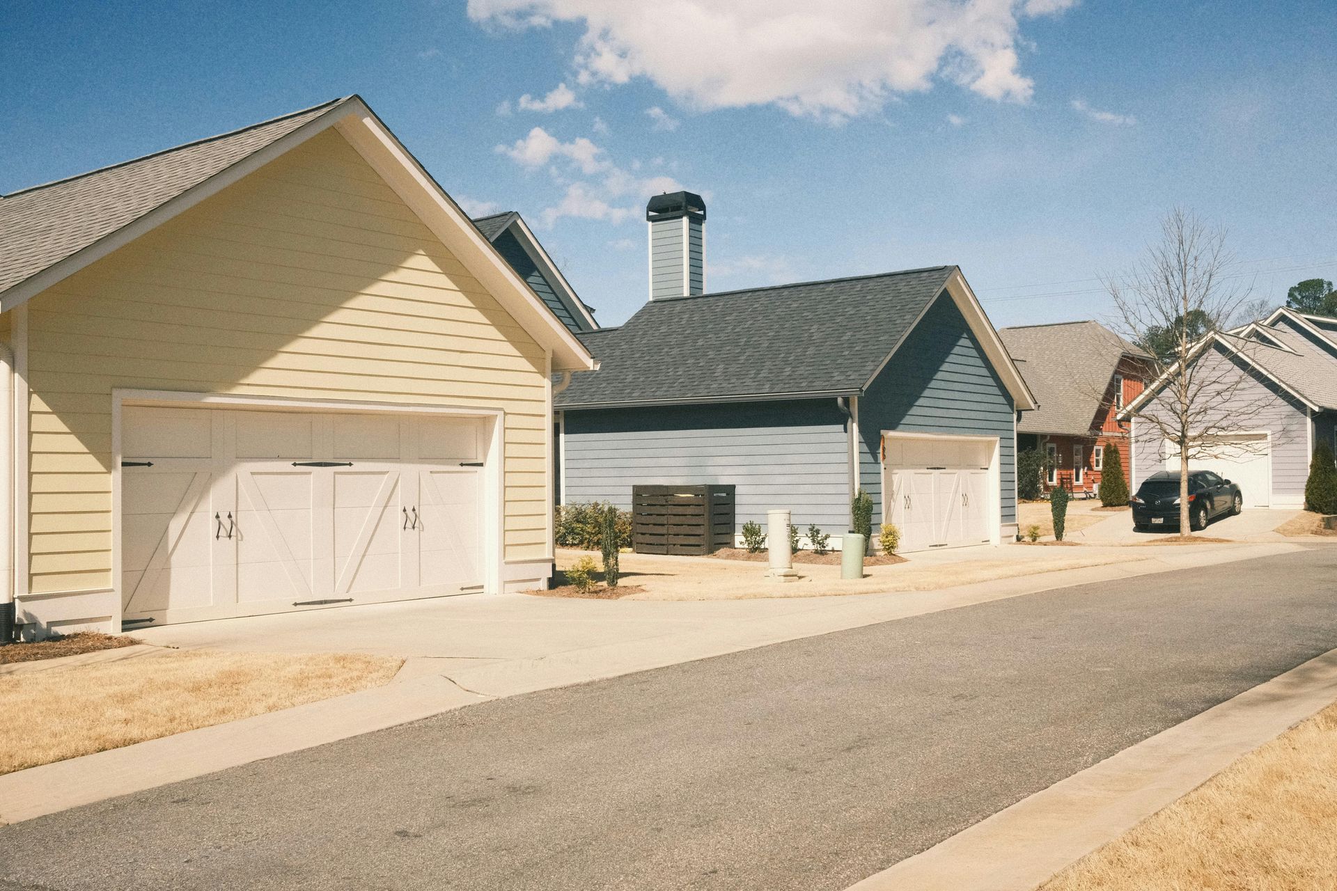 Row of houses with garages, blue sky, and a street.