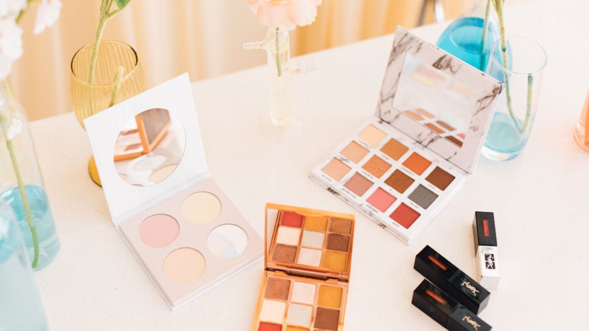 Un tocador blanco con brochas de maquillaje en soportes transparentes, tarros de cosméticos.