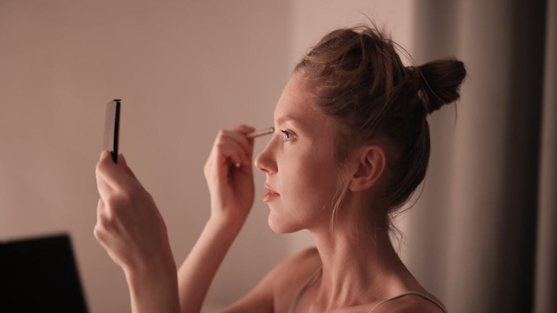 Una maquilladora profesional aplica sombra de ojos a una clienta en un estudio luminoso.