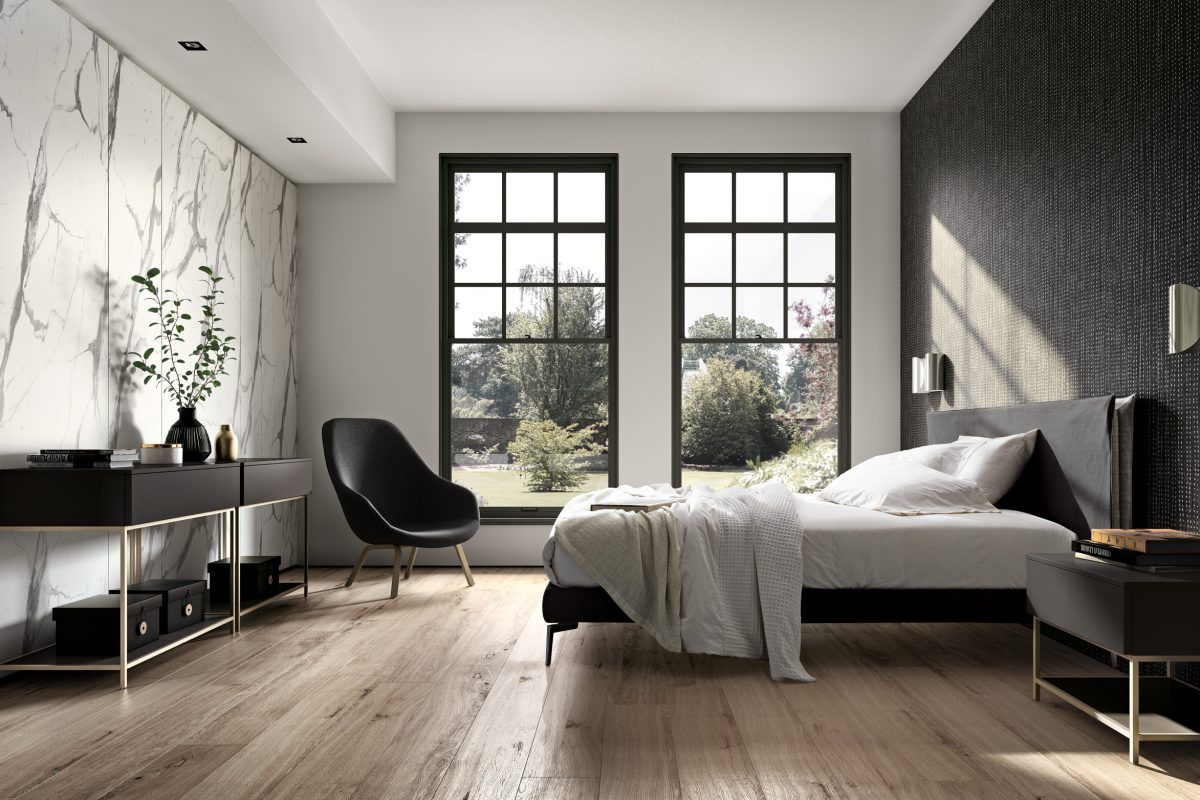 Una camera da letto con un letto, una sedia, un comodino e due finestre.