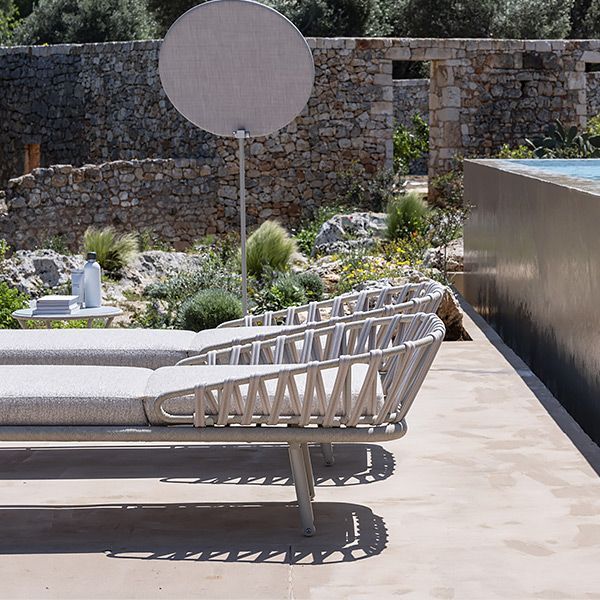 Una fila di sedie a sdraio sono disposte su un patio accanto a una piscina.