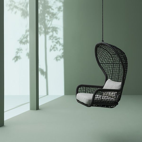 Una sedia sospesa in vimini nero con un cuscino bianco