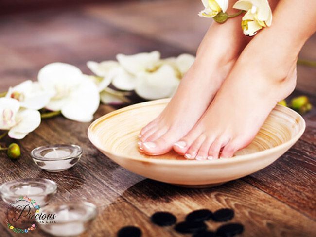 De voeten van een vrouw staan in een kom met water met bloemen.