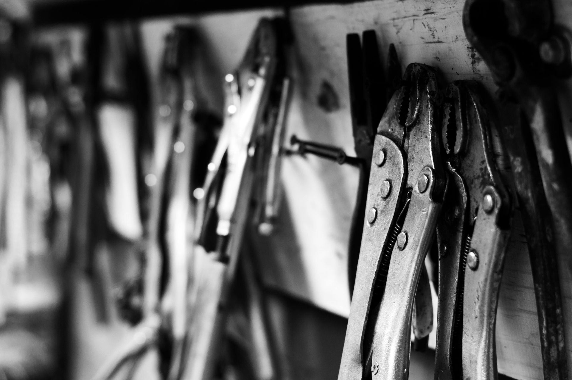 Metal tools, primarily pliers, hanging on a wall in black and white.