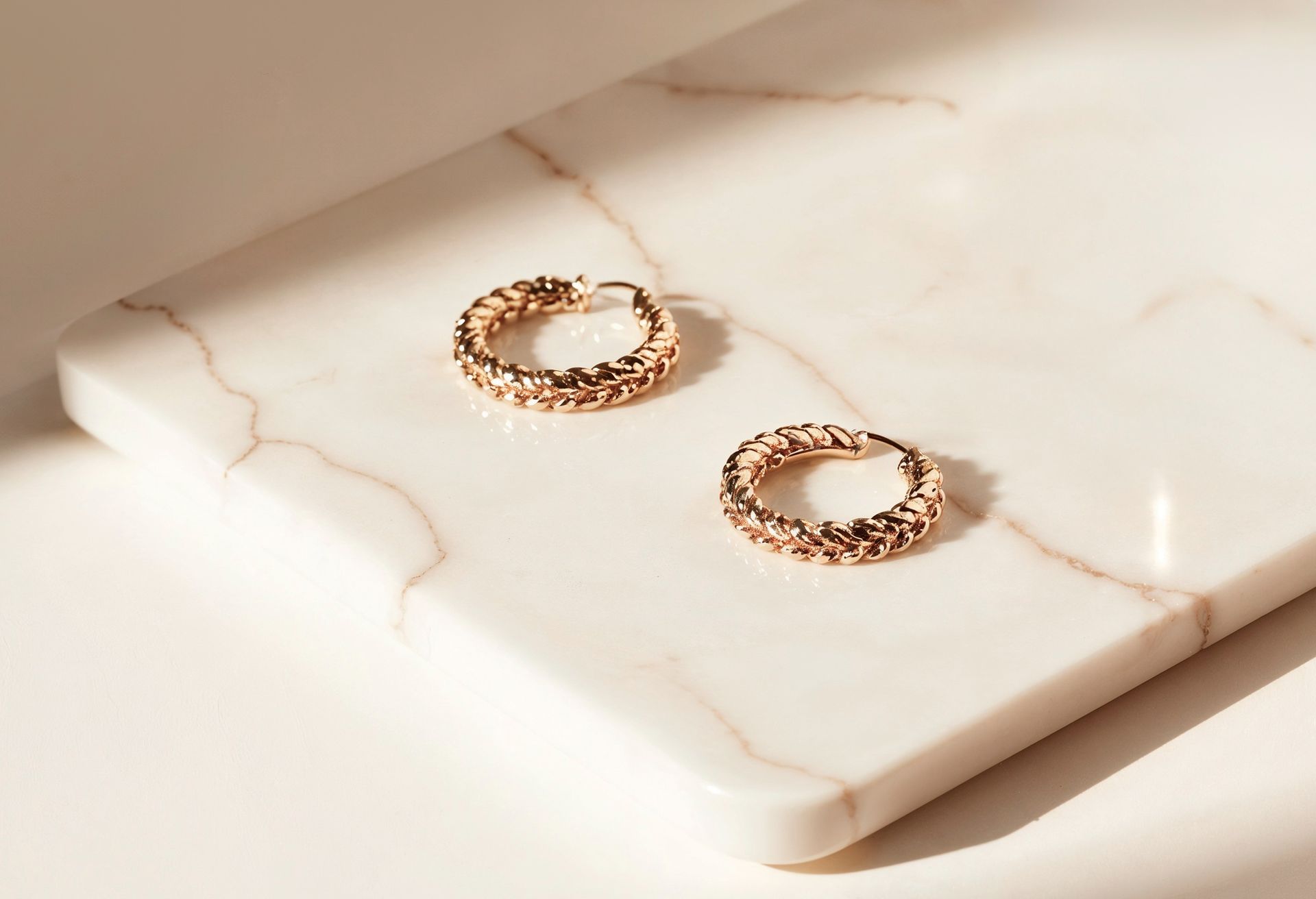 Par de pendientes de aro de oro sobre superficie de mármol.