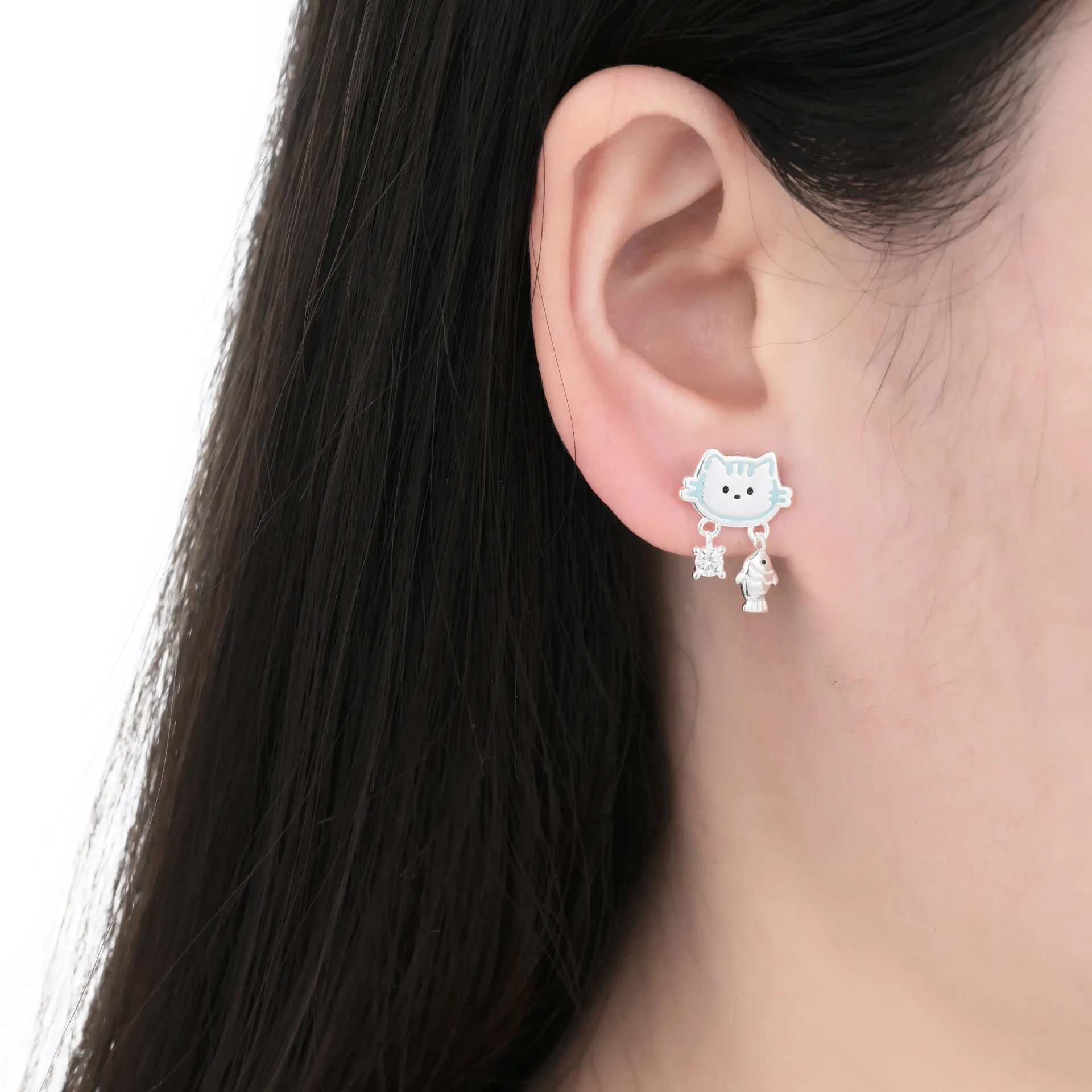 Primer plano de la oreja de una persona con un pendiente de plata en forma de gato con un pez colgando.