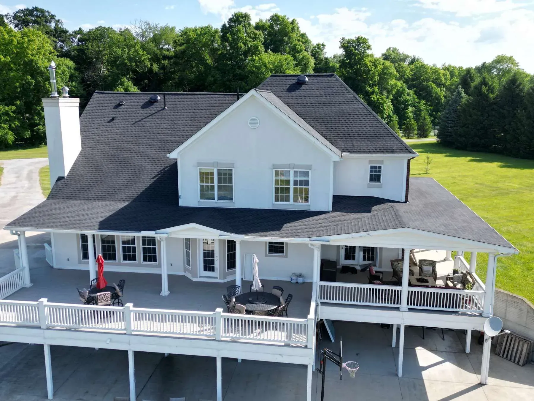 Two-story white house with a black roof, wraparound porch, and large yard under a blue sky.