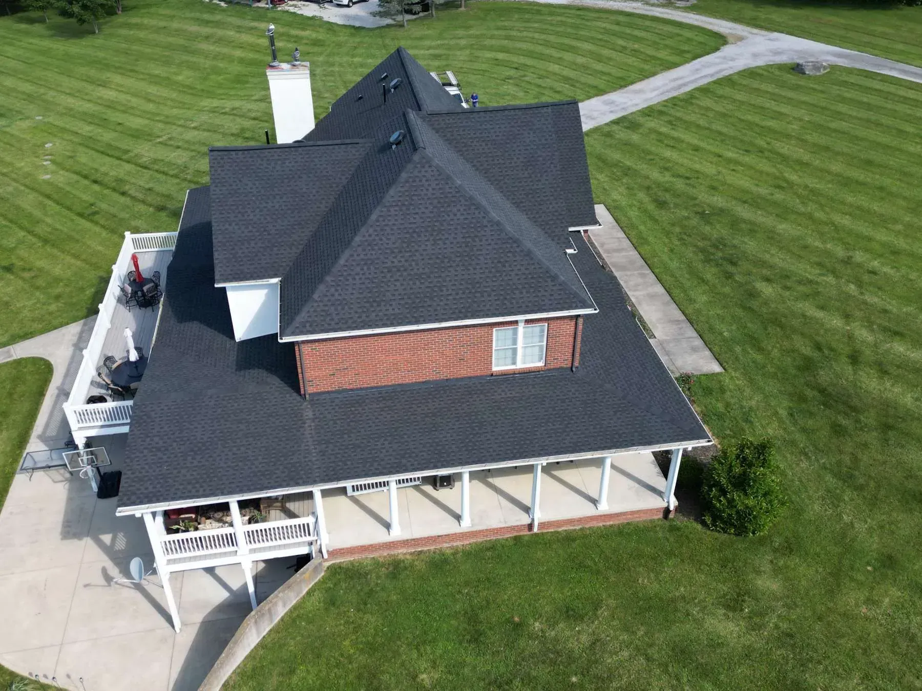 Aerial view of a house with a dark roof and brick chimney, surrounded by green grass.