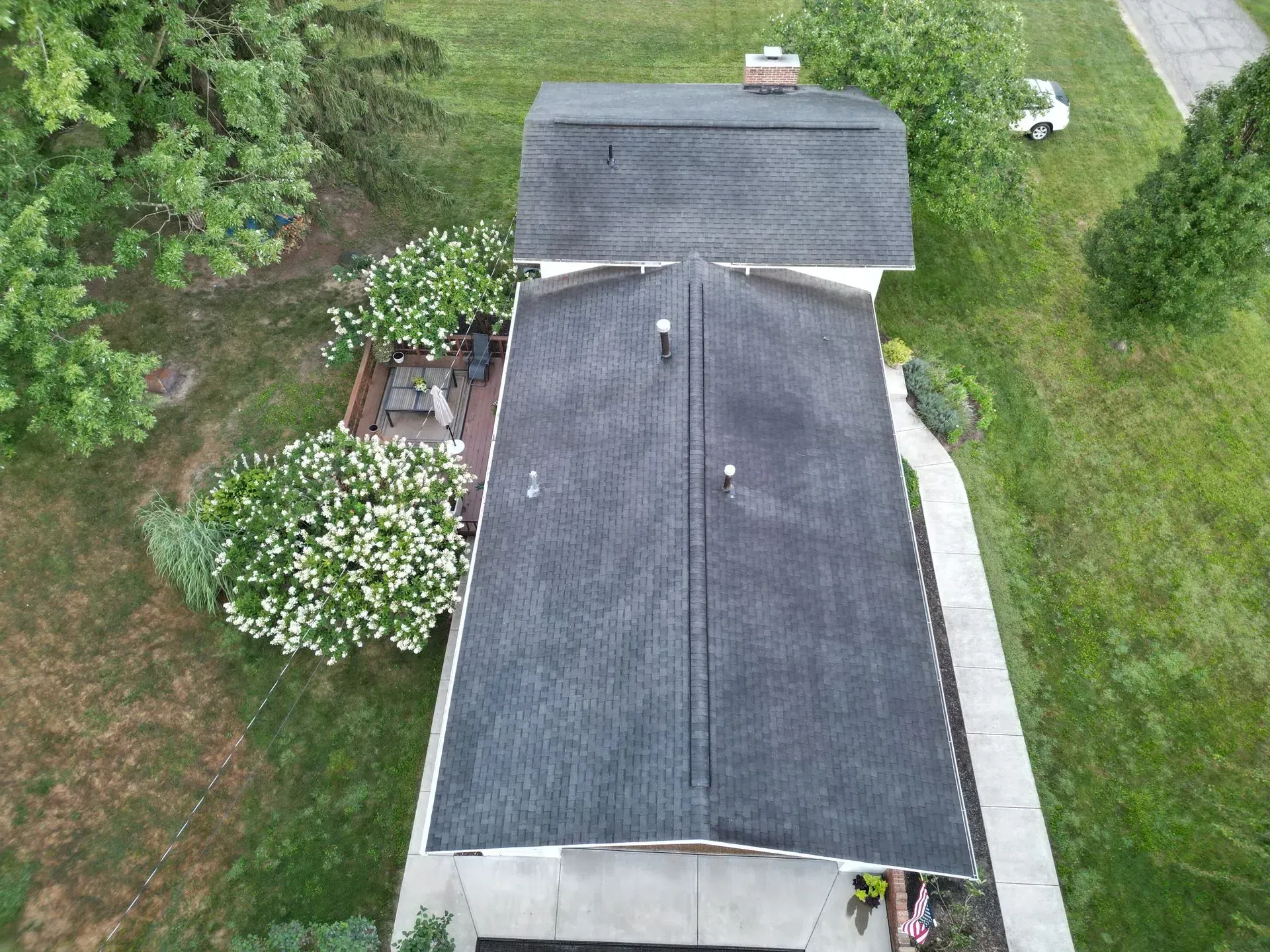Overhead view of a house with a dark gray roof surrounded by green grass and trees.