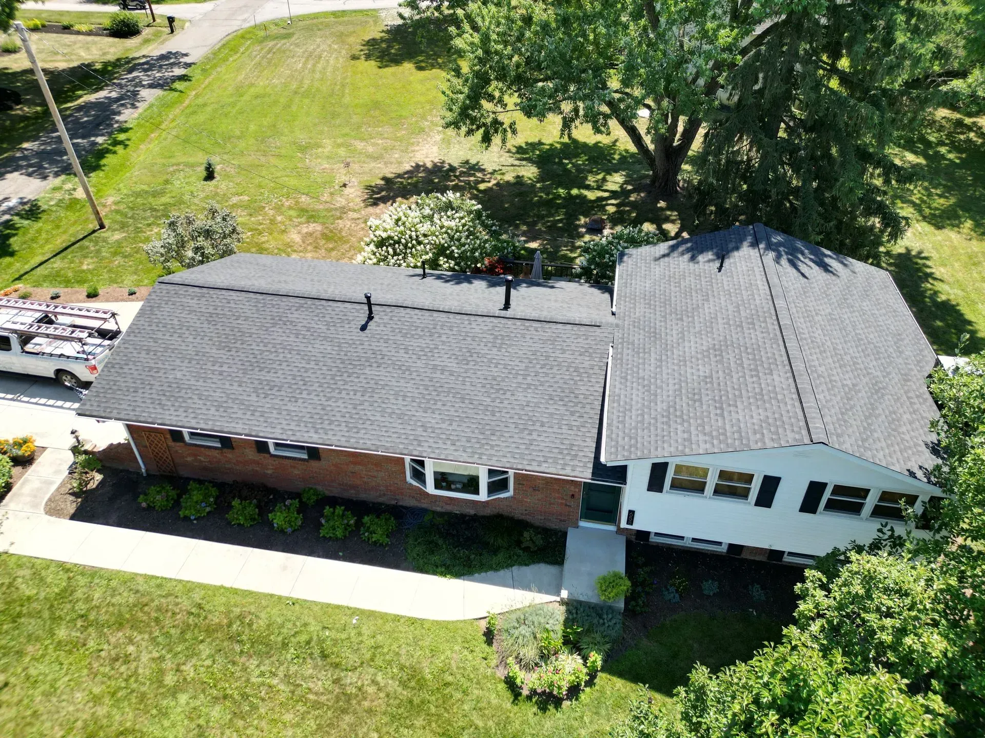 Aerial view of a house with a new dark gray roof and green yard.