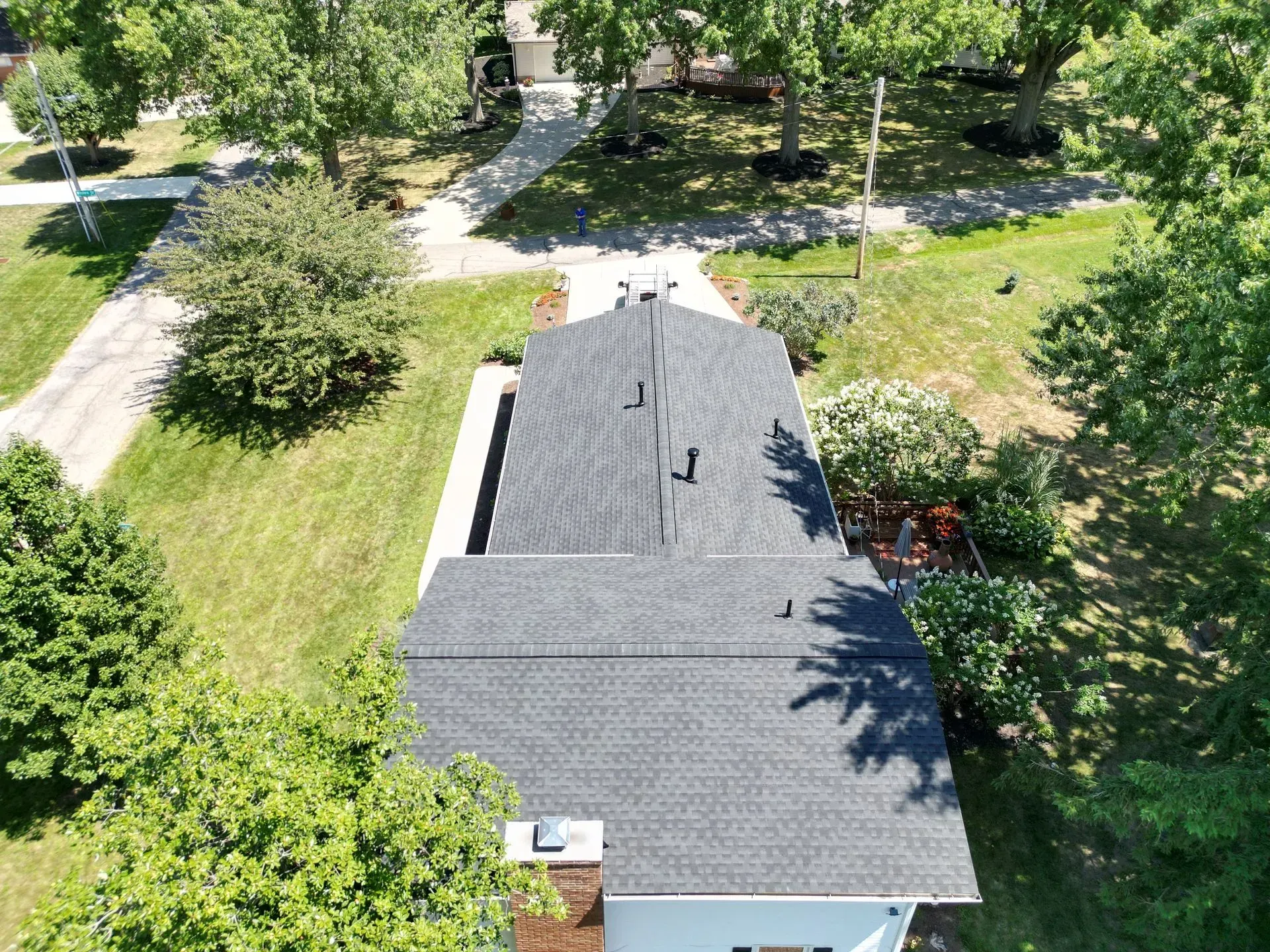 Overhead view of a house with a dark gray shingle roof, surrounded by green grass and trees.