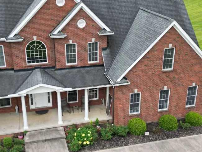 White gutters and downspout on a corrugated metal building with red roof, against a cloudy sky.
