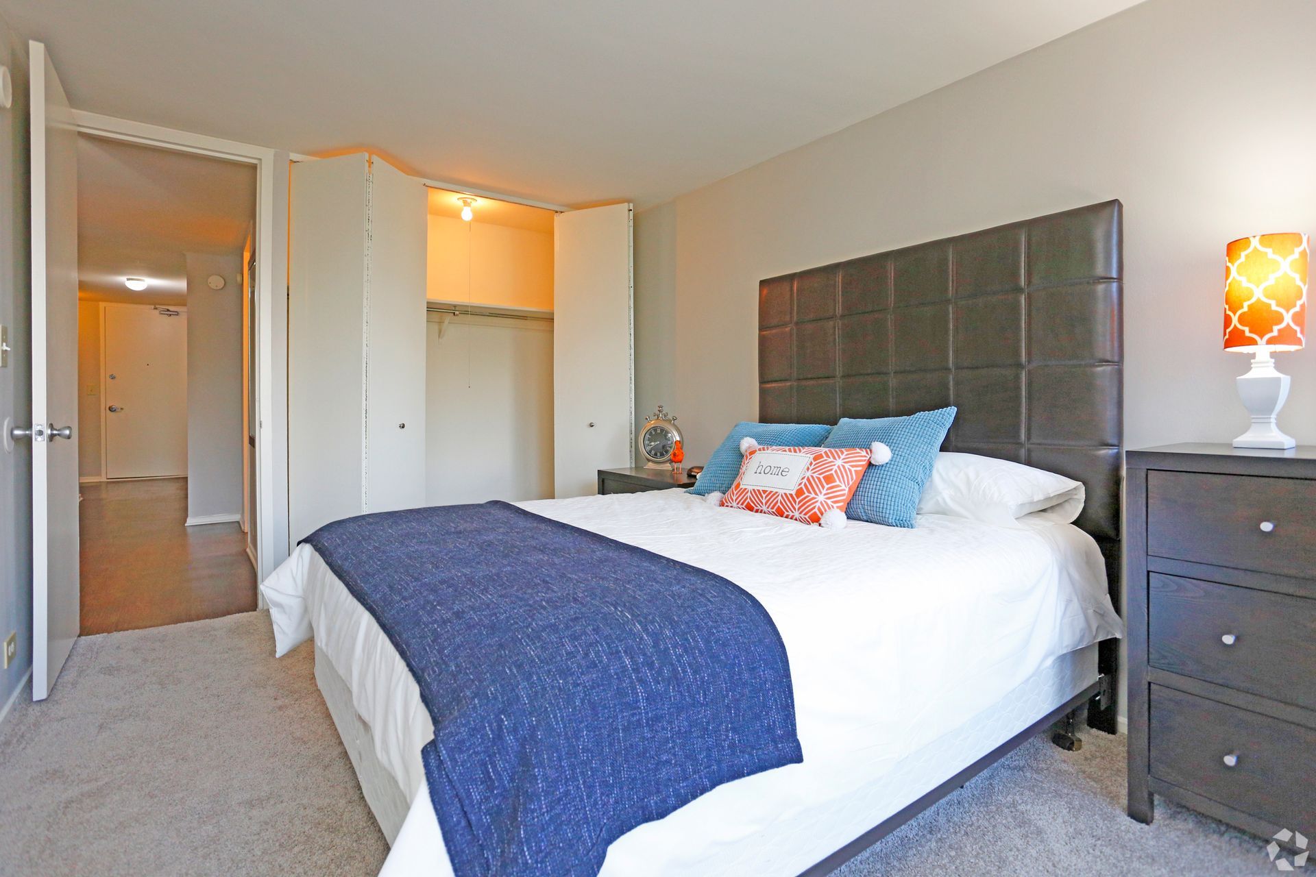 Bedroom with a bed, closet, and dresser. The bed has blue bedding and decorative pillows. Gray walls and carpet.