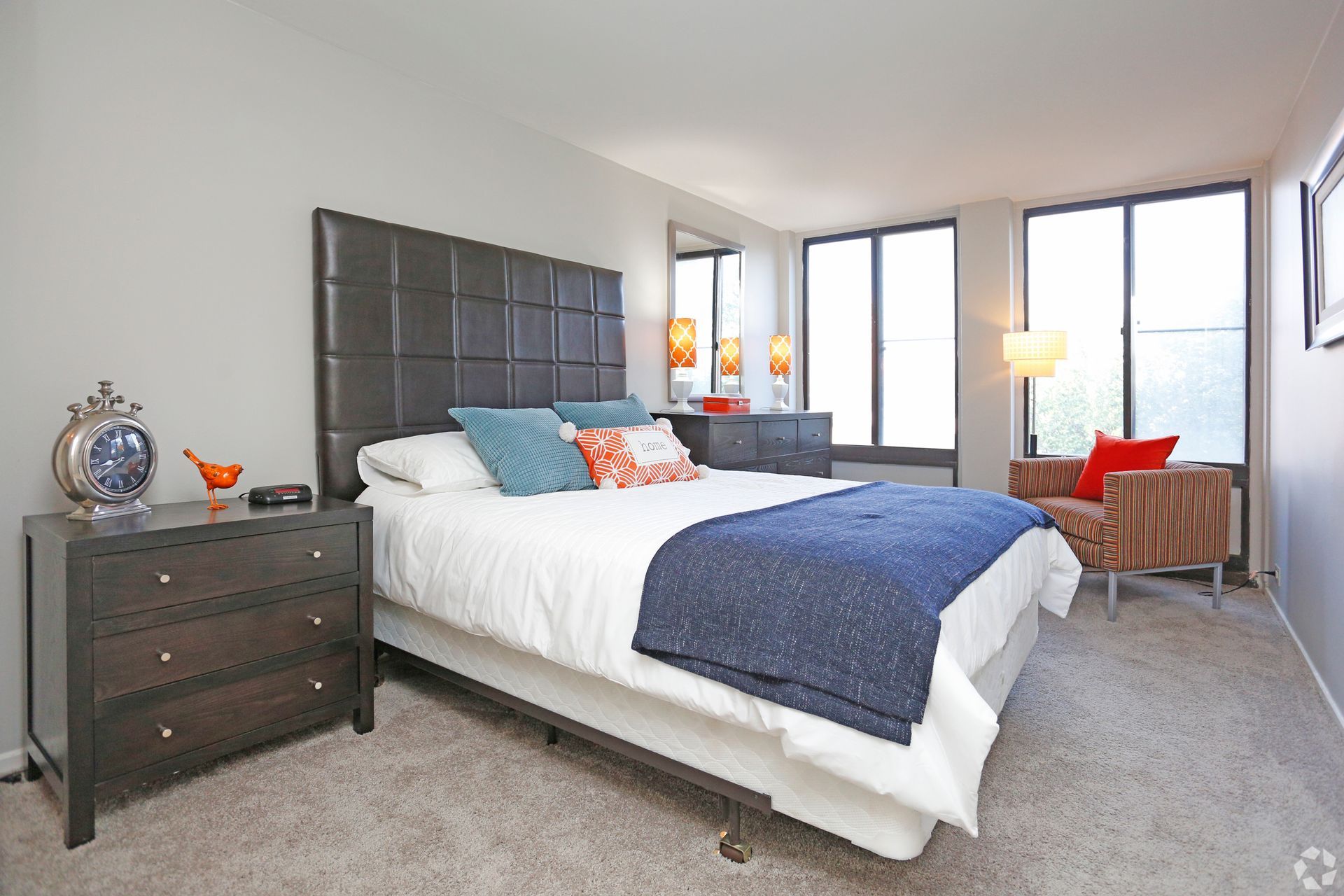 Bedroom with a bed, nightstand, dresser, windows, and armchair. Gray walls, neutral carpet.