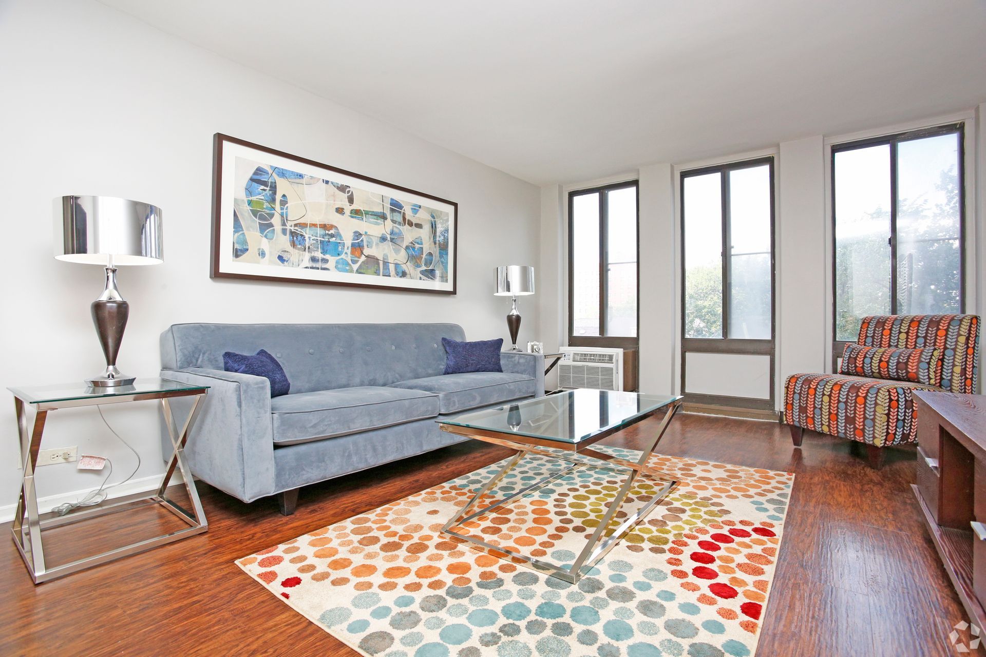 Living room with blue sofa, patterned rug, picture, glass table, and arm chair.