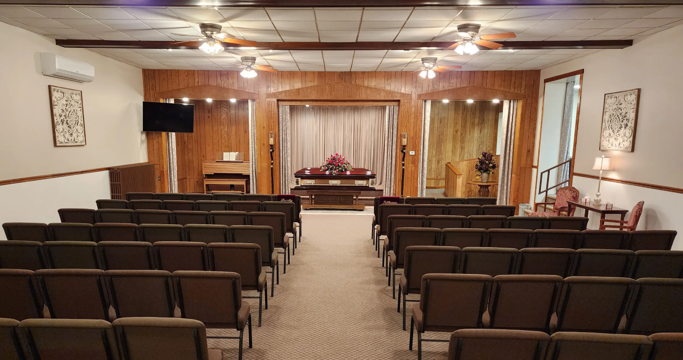 A funeral home with rows of chairs and a coffin in the middle of the room.