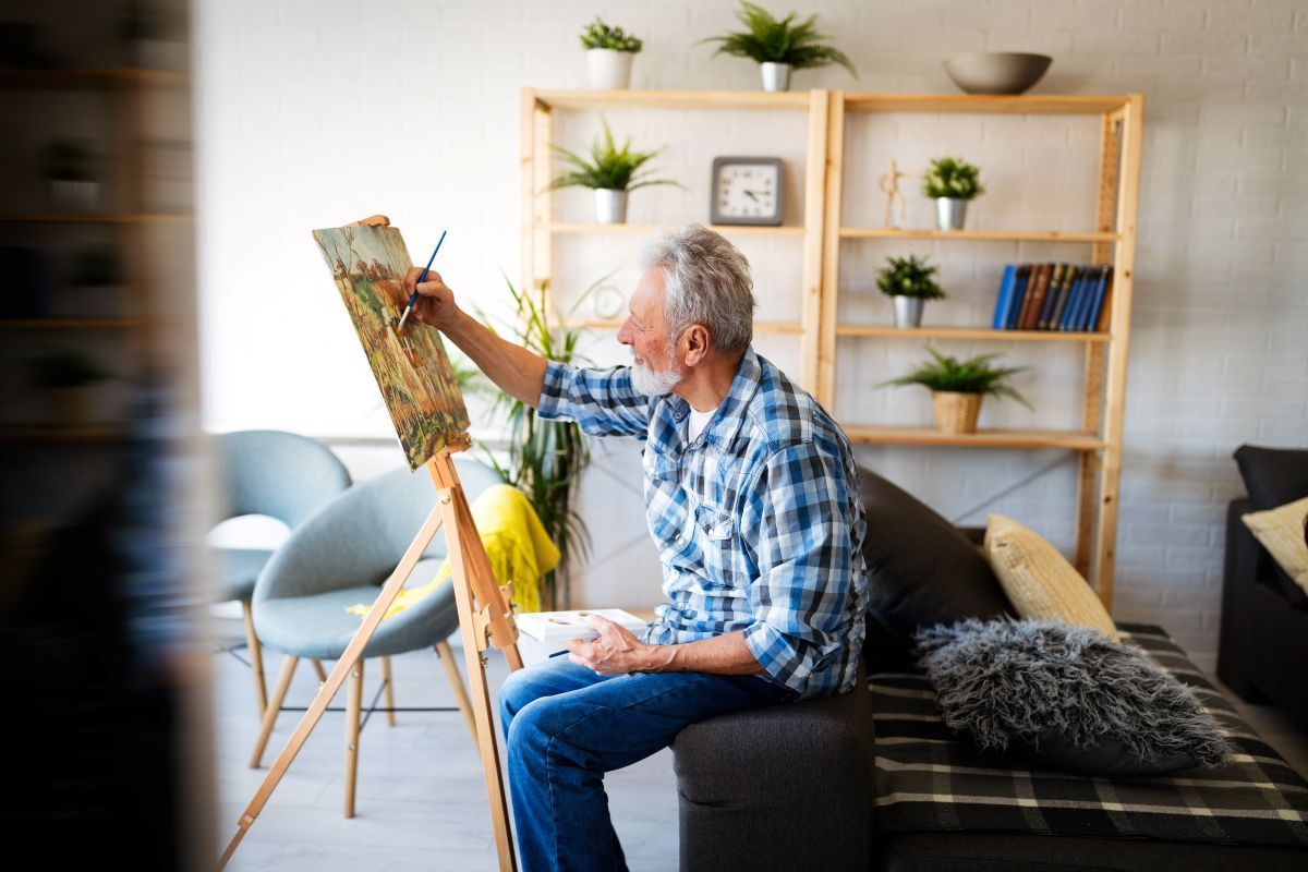A man is sitting on a couch painting a picture on an easel.