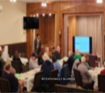 Blurred photo of several people seated at tables in large room
