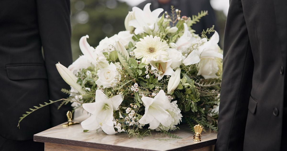 A coffin with a bouquet of white flowers on top of it.