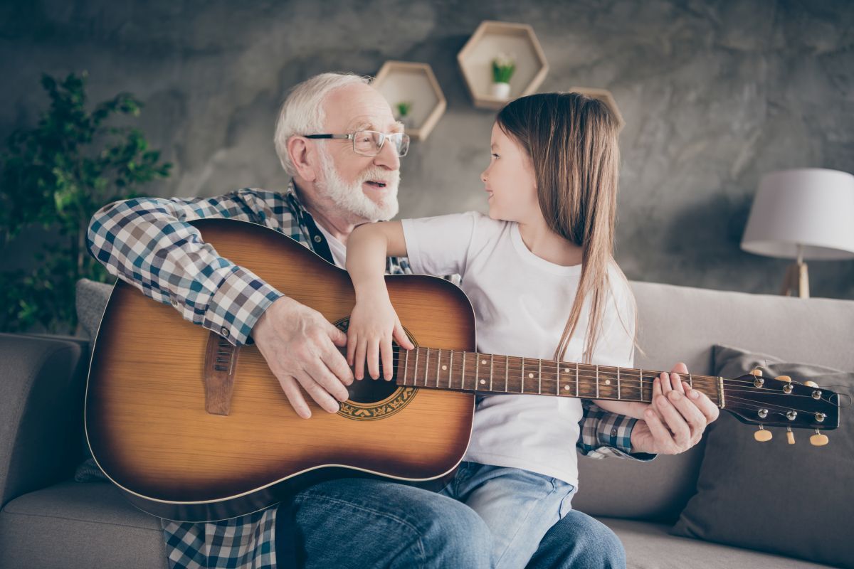 A man and a little girl are sitting on a couch playing a guitar.