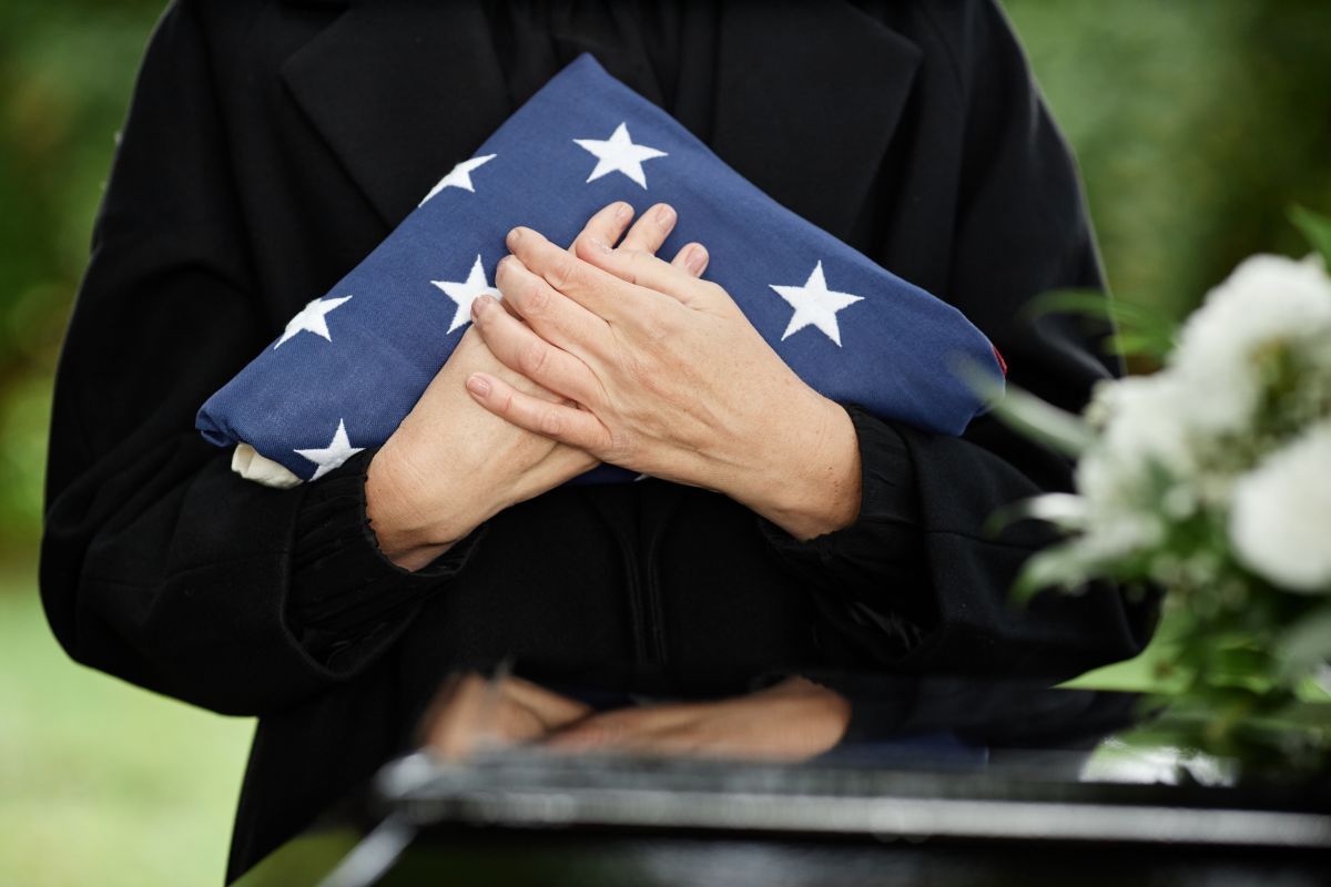 A woman is holding an american flag in her hands at a funeral.