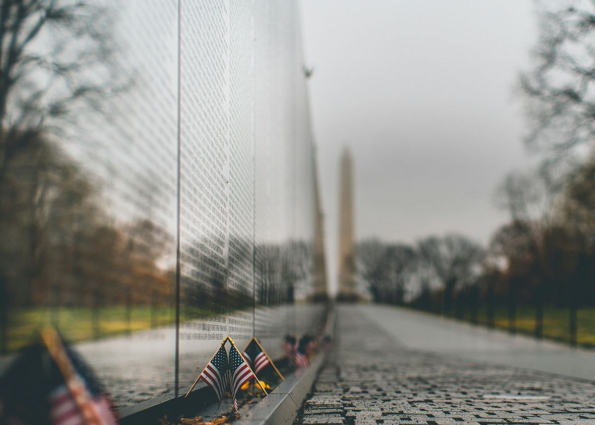 A row of american flags are sitting on a wall in front of a memorial.