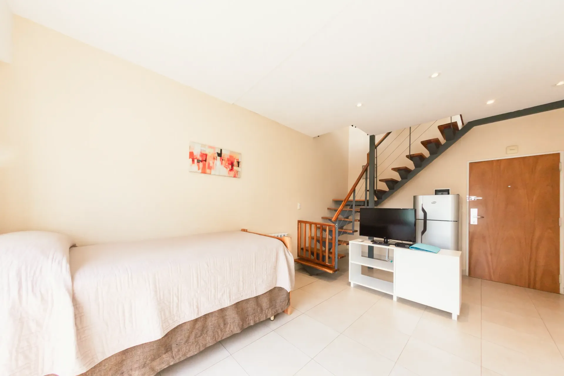 Un dormitorio con una cama, televisión y escaleras.