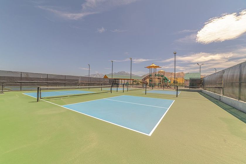 Tennis court with blue playing surface, playground in the background, blue sky.
