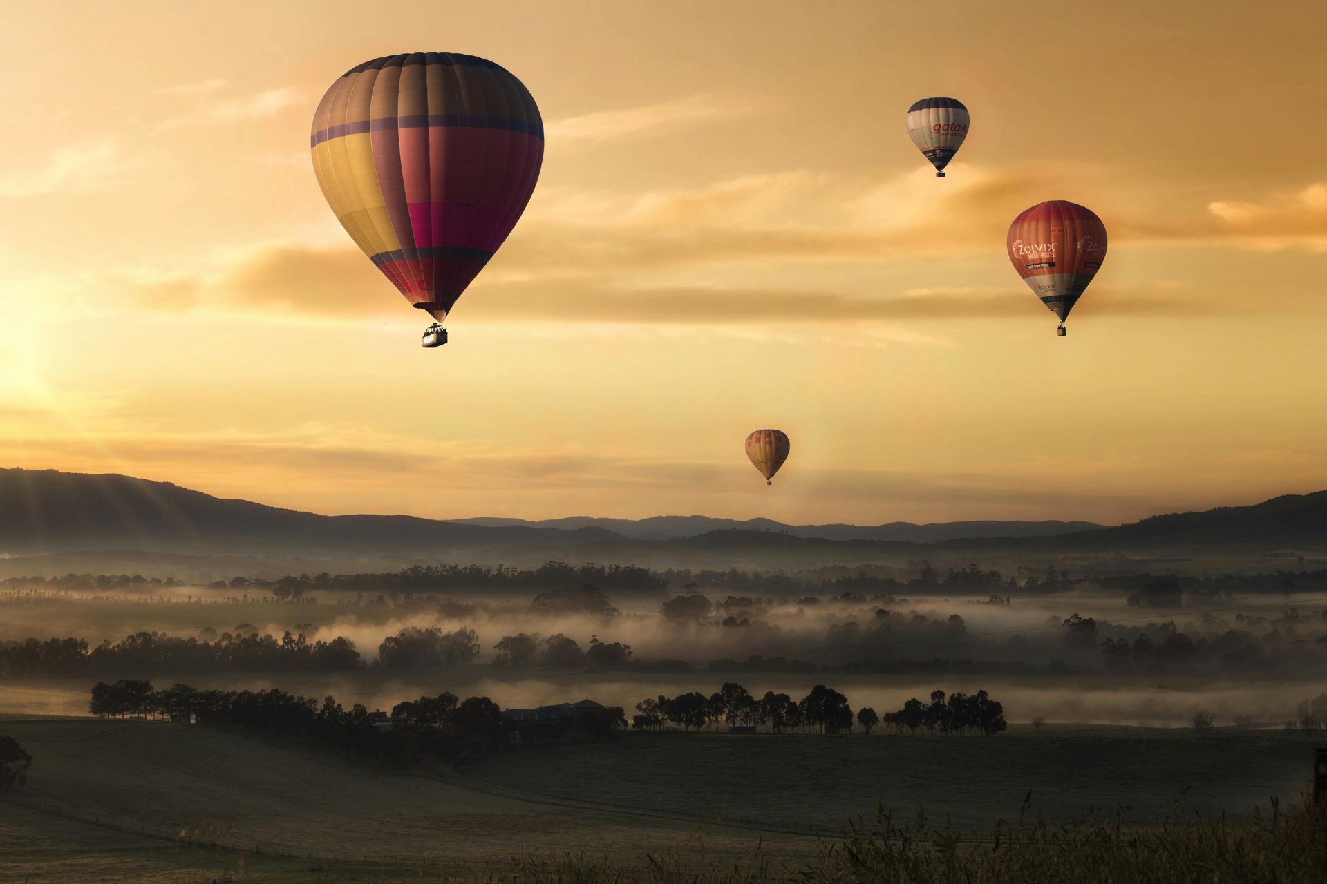 Hot air balloons float over a misty valley at sunset.