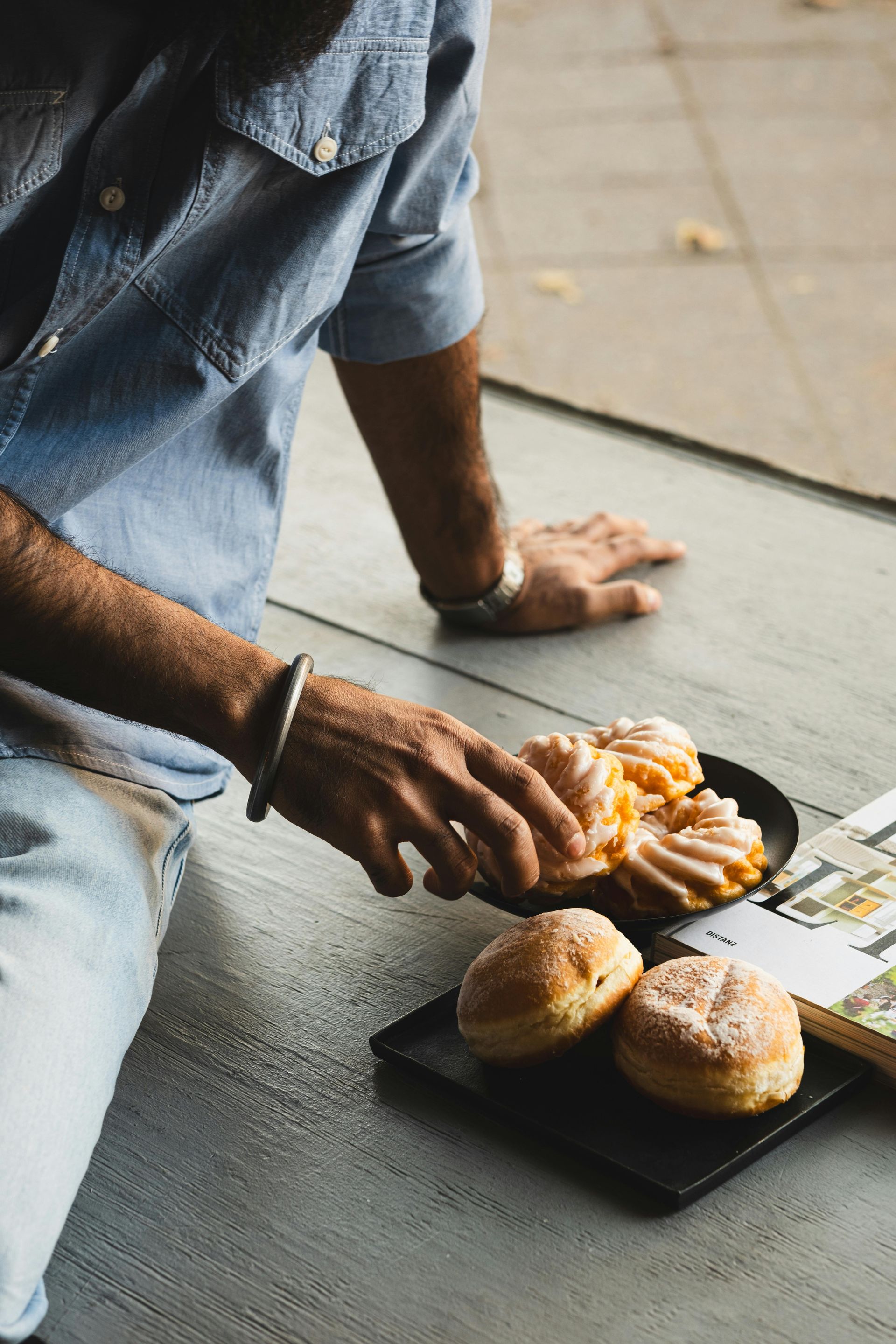 Person reaching for pastries on a black plate, sitting on a wooden floor.