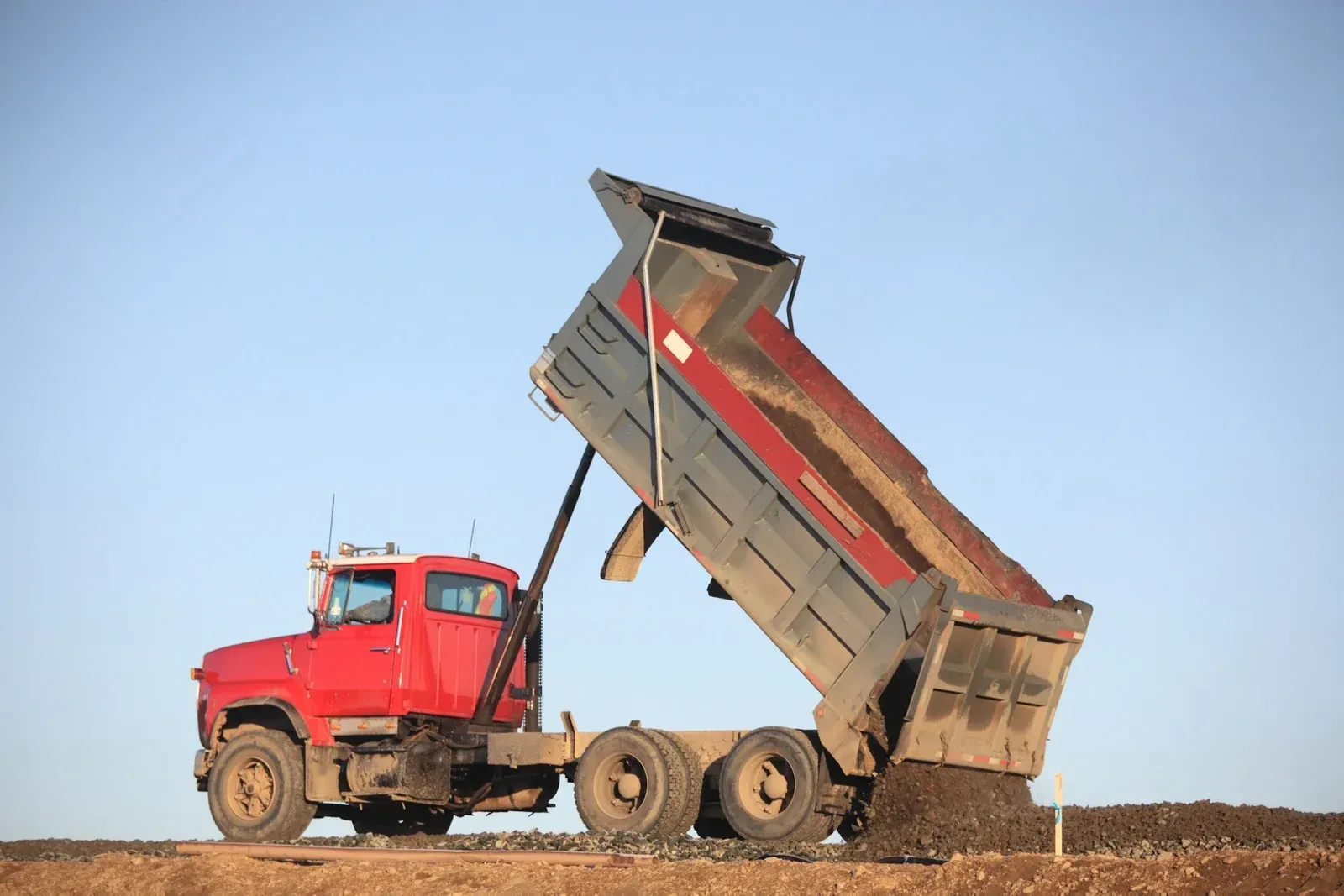 A red dump truck is dumping dirt into a field.