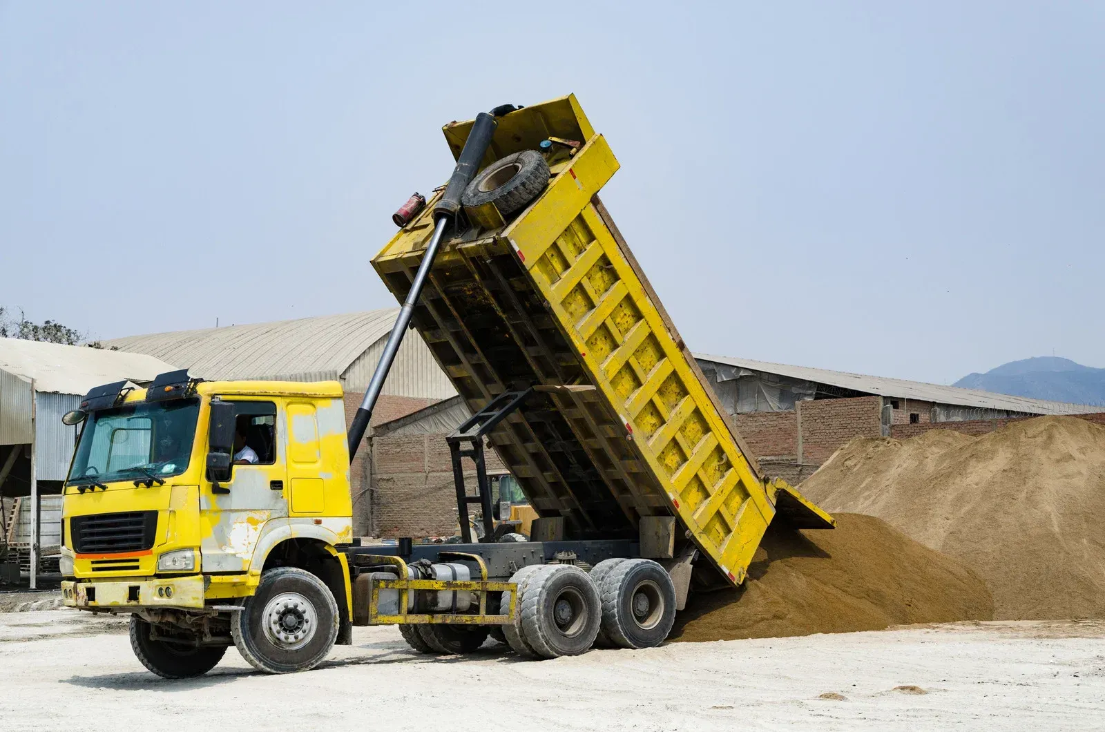 A yellow dump truck is dumping dirt into a pile of dirt.