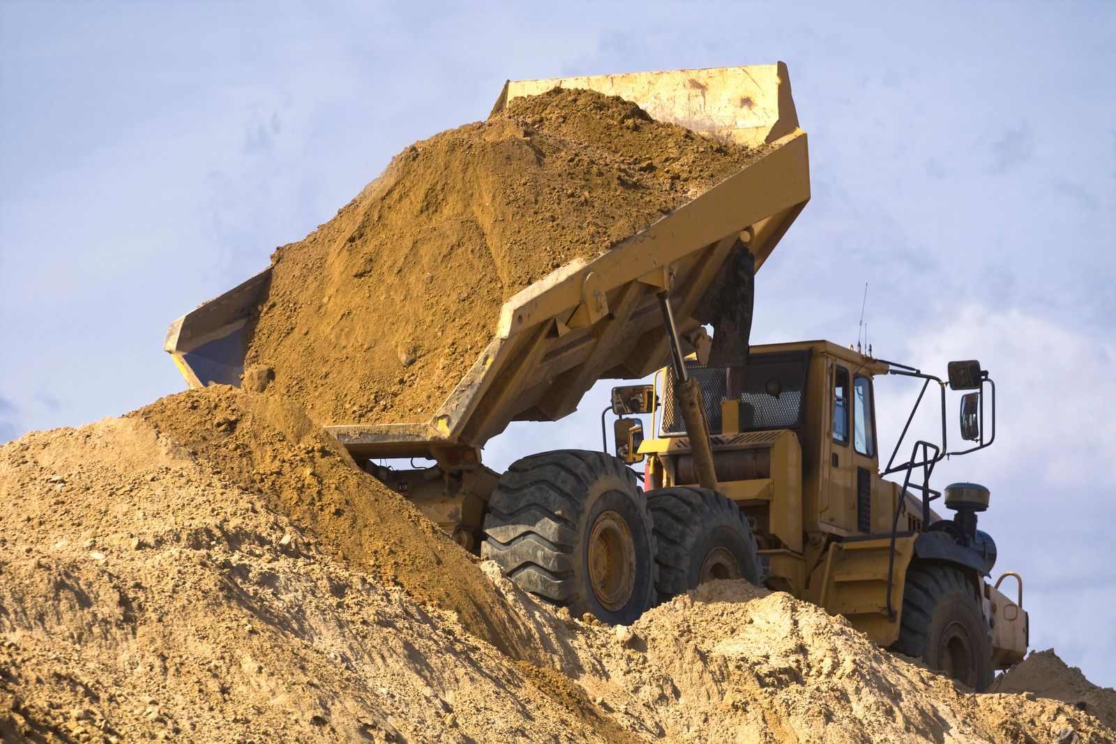 A dump truck is dumping dirt into a pile of dirt.
