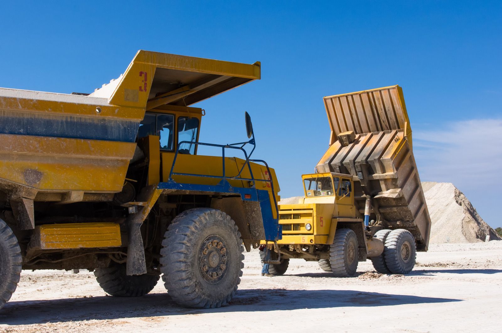 Two yellow dump trucks are parked next to each other in a dirt field.