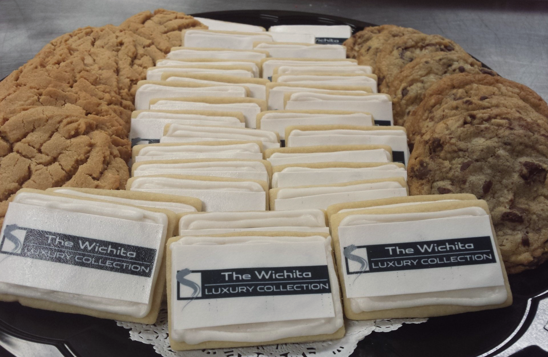 A cookie tray with chocolate chip cookies and rectangular sugar cookies with logos in the icing