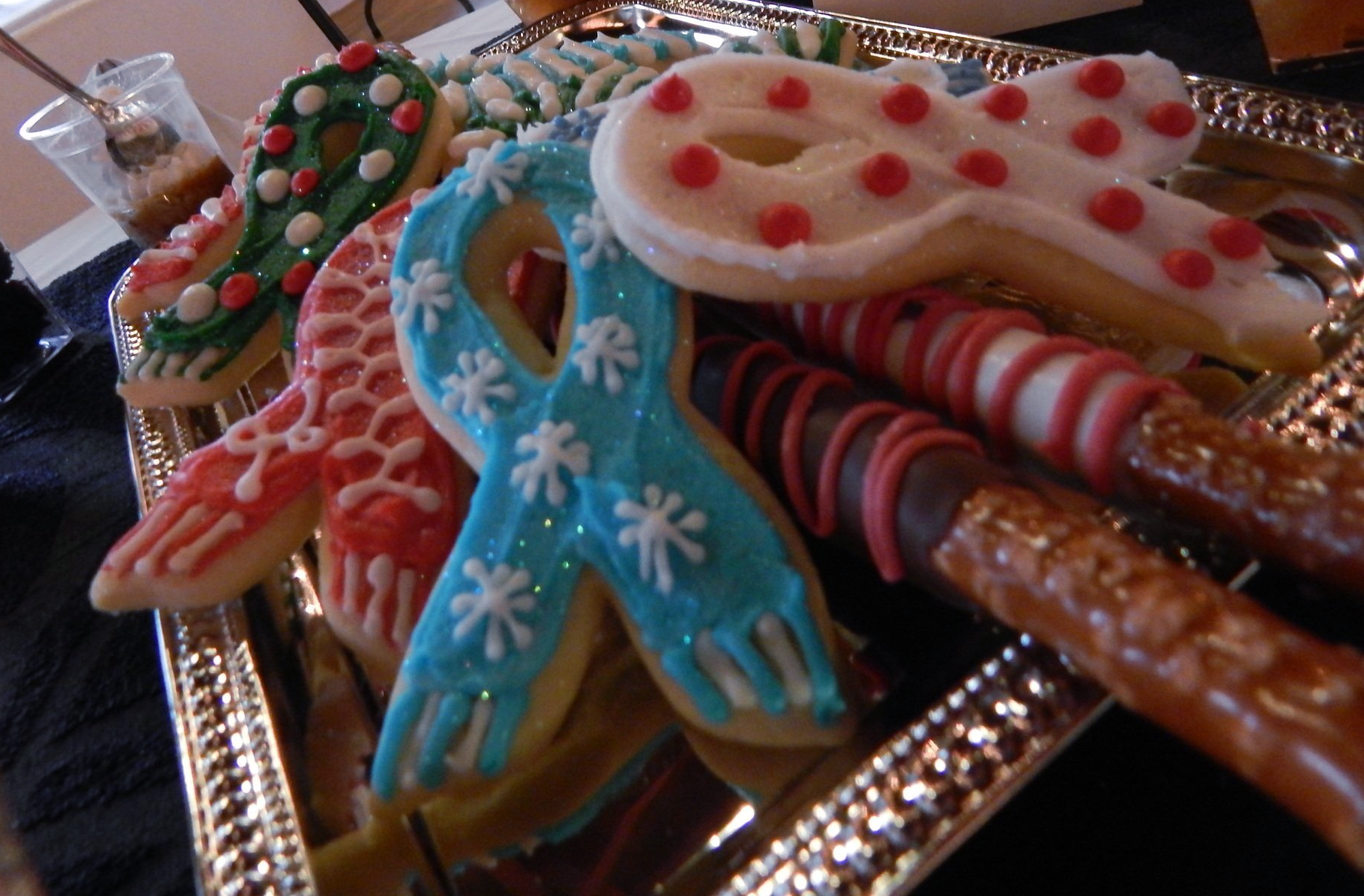 A party tray with dipped pretzel rods and iced sugar cookies shaped like ribbons