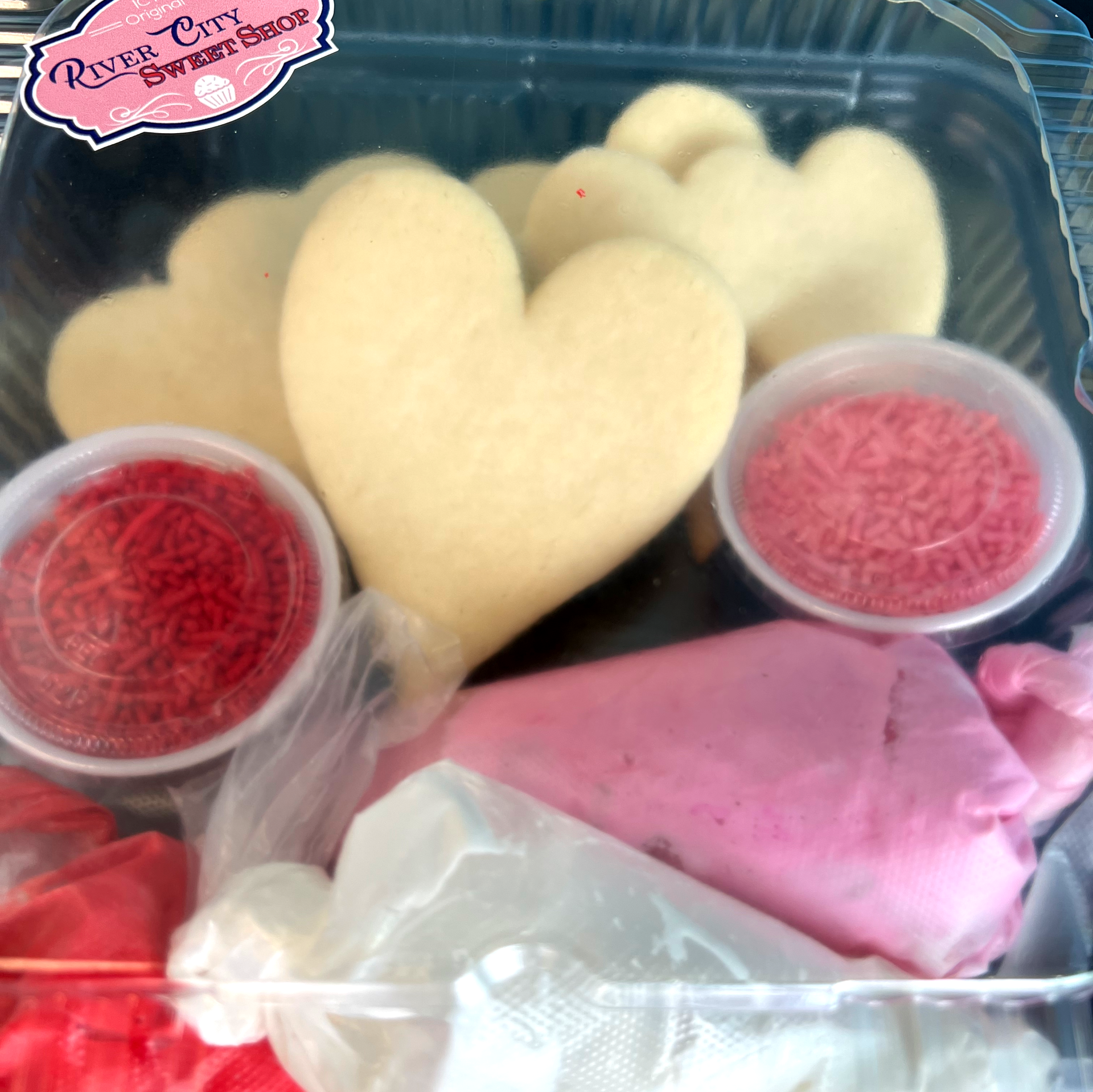 A box with cups of sprinkles, small bags of icing, and plain heart shaped sugar cookies