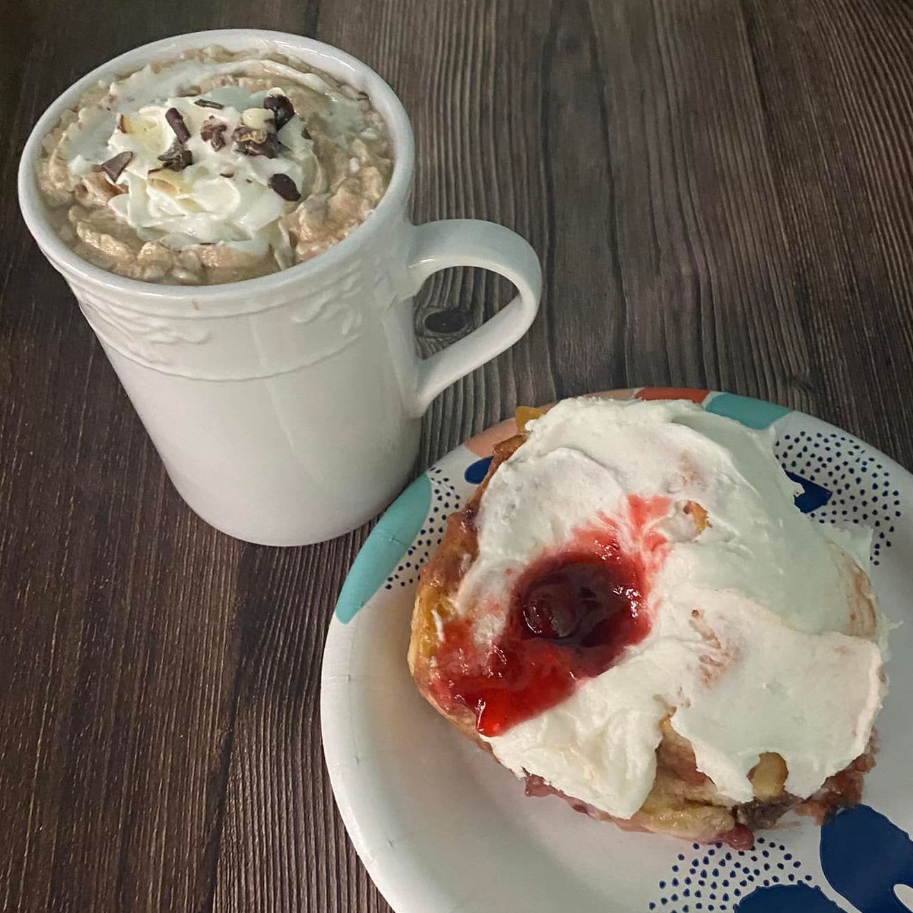 A strawberry cream cheese cinnamon roll on a plate and a mug with a mocha coffee