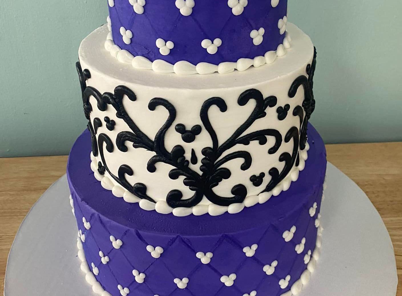 A tiered cake iced in white and purple with black swirls