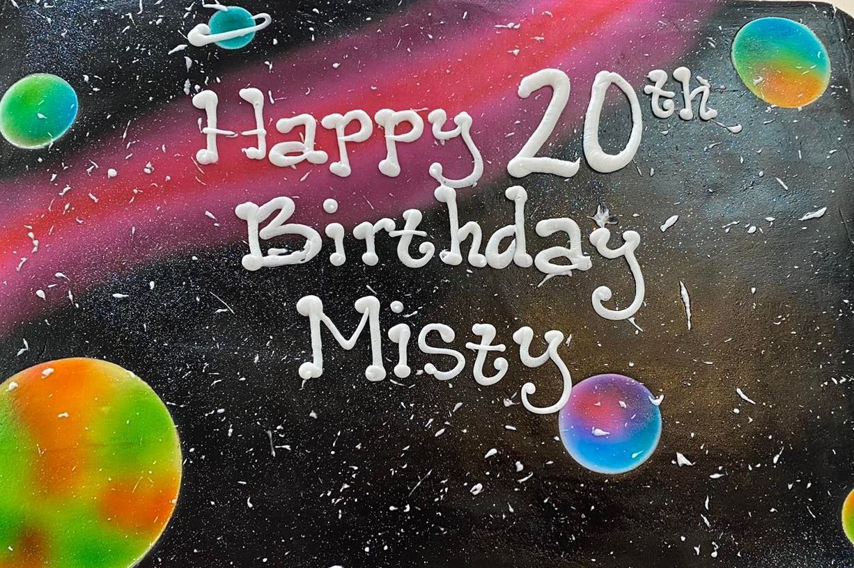 A sheet cake iced in a galaxy theme with Happy Birthday written on it