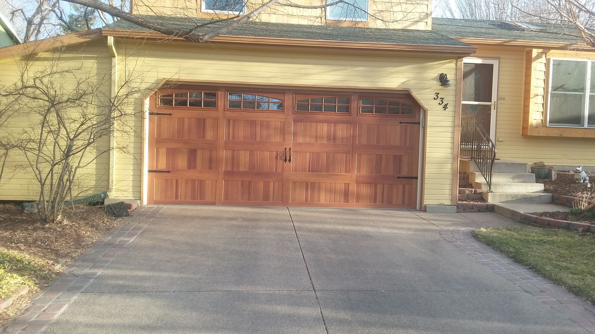 Garage with brown door and yellow siding on a house with a concrete driveway.