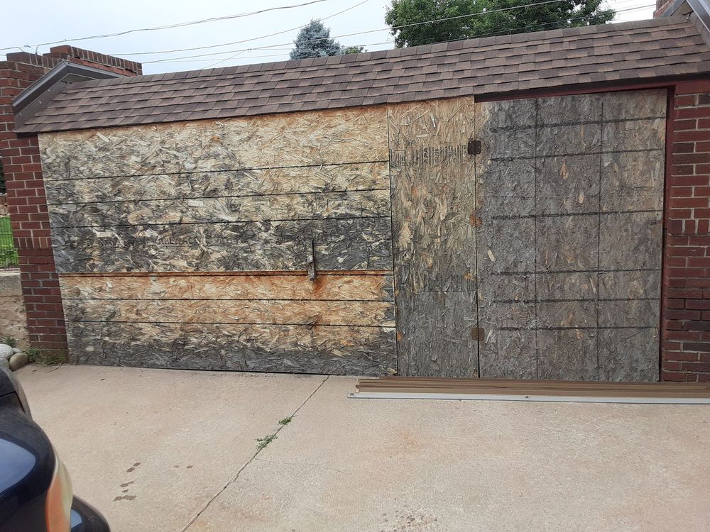 Weathered wooden shed with brick walls and a brown shingle roof, boarded up.
