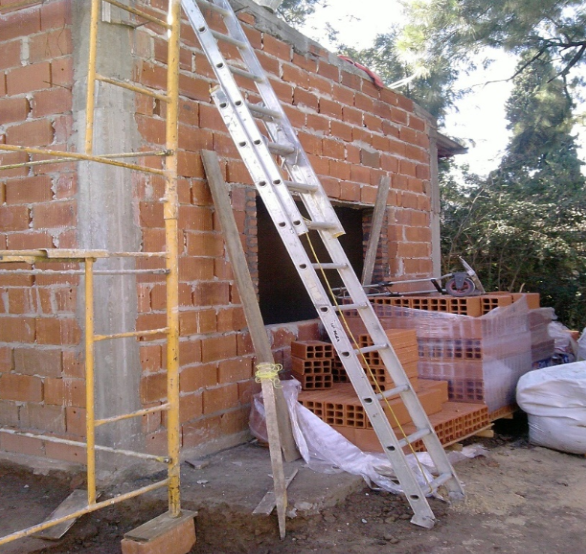 Edificio en construcción con fachada de ladrillo, escalera y andamios.
