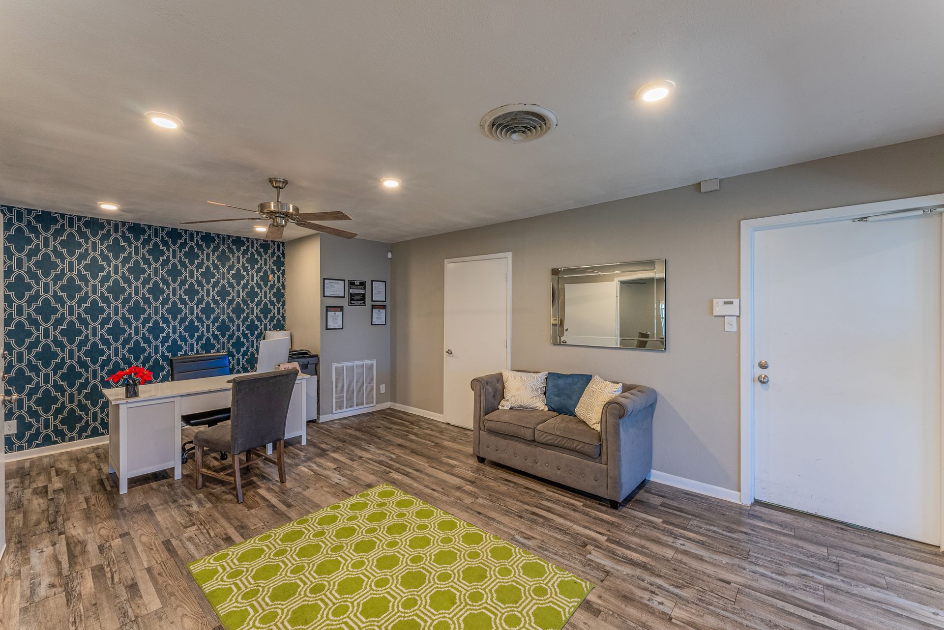 A living room with a couch , desk , chair and ceiling fan.