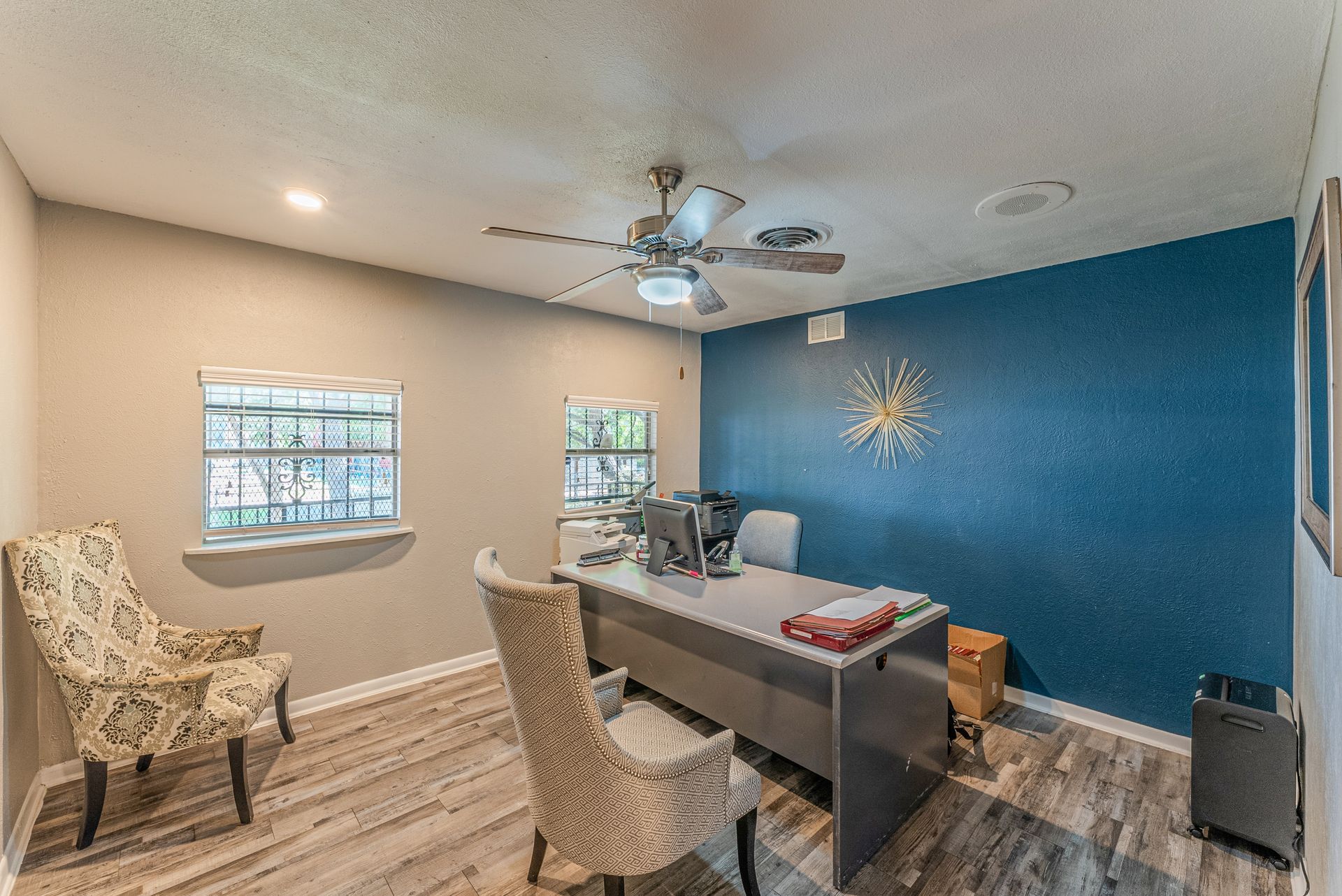 A room with a desk , chairs , and a ceiling fan.