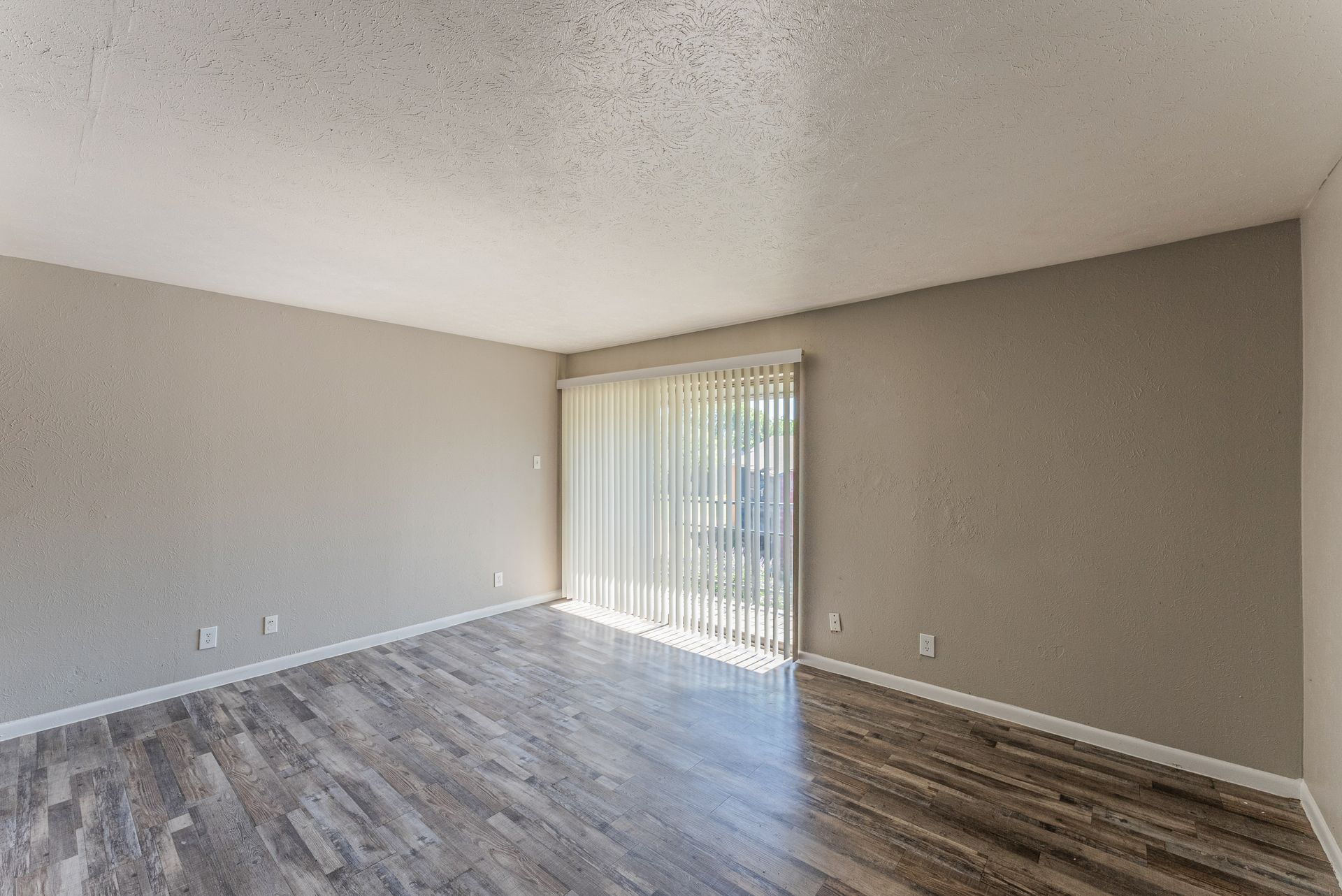 An empty living room with hardwood floors and a sliding glass door.