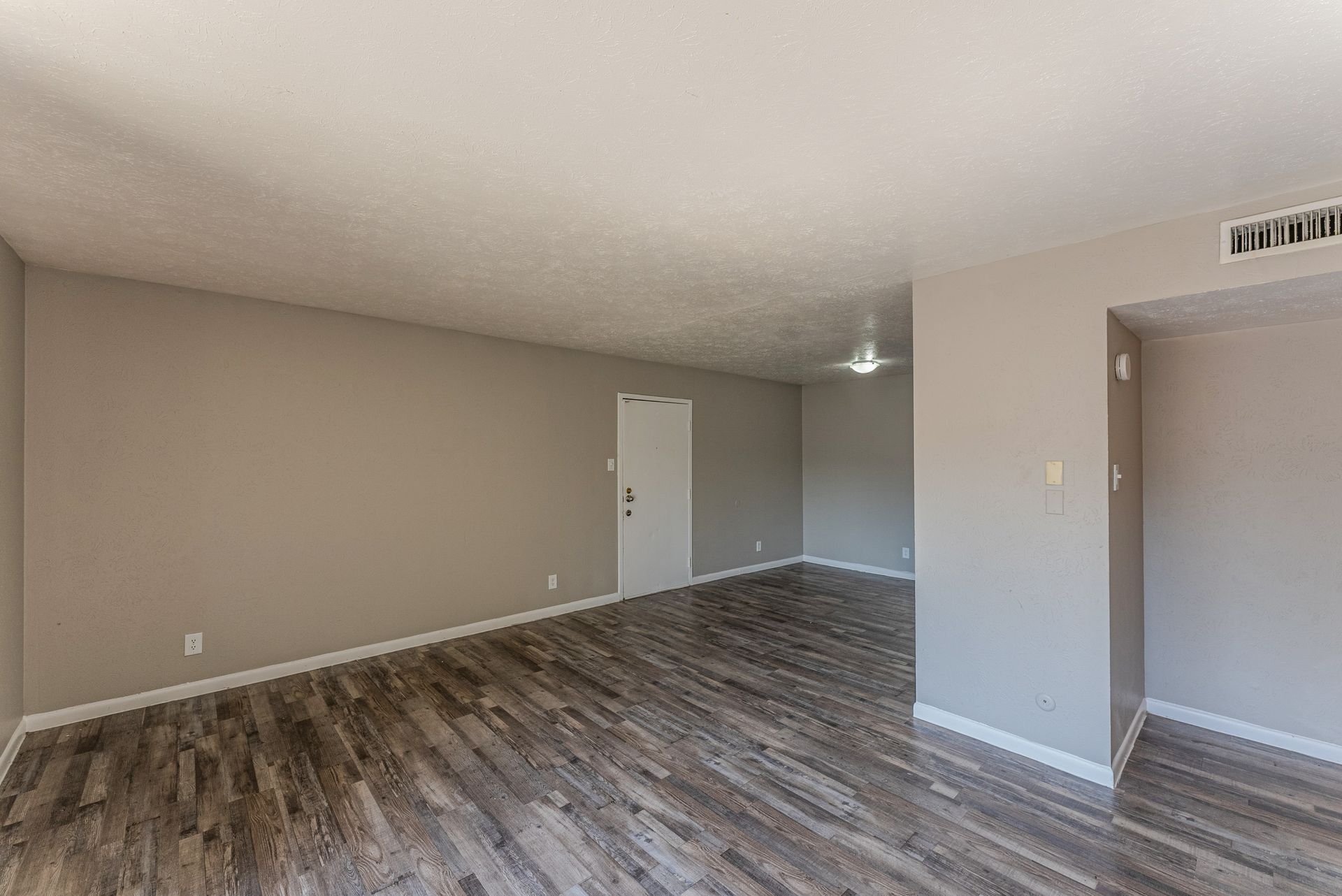 An empty living room with hardwood floors and gray walls.
