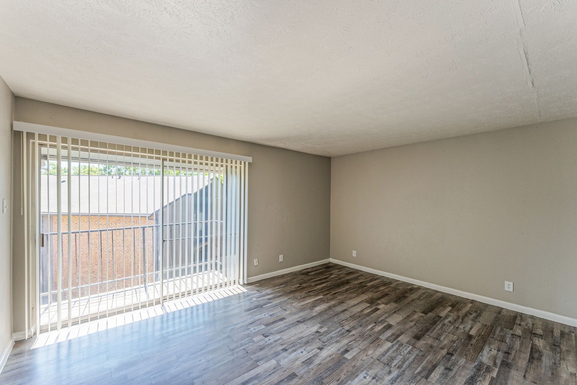 An empty living room with hardwood floors and sliding glass doors.